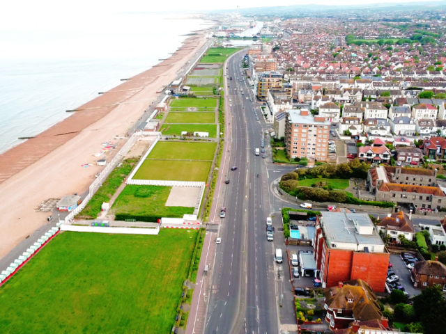 a road with green spaces, houses and the sea
