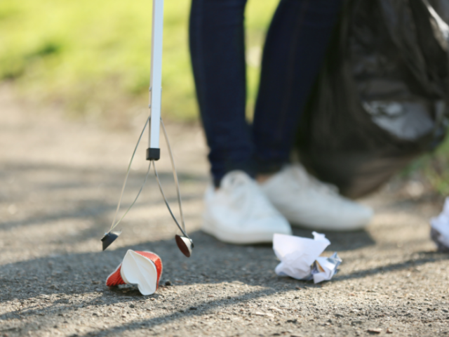Photo of a person wearing jeans and white trainers using a litterpick to pick up rubbish. 