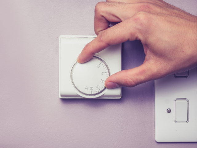 A photo of a person adjusting a thermostat