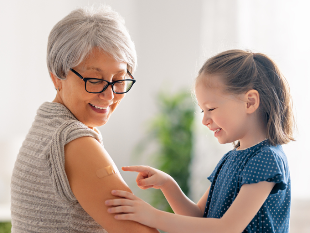 young girl points to a plaster on an older woman's right arm