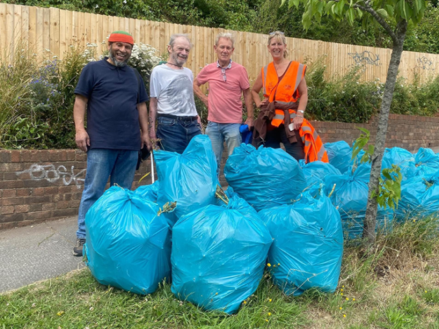 Photograph of 4 people smiling behind a pile of blue bags of litter.