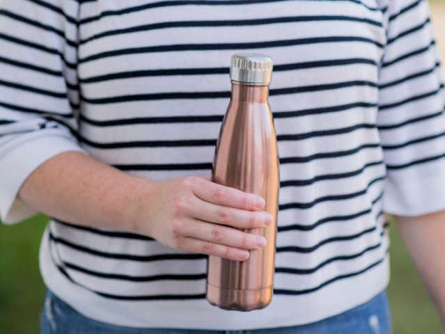 A photo of a person in a stripey jumper holding a refillable water bottle.