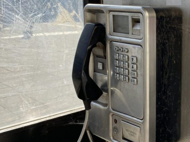 A British Telecom on-street payphone mounted on the inside wall of its phone booth. The black received is mounted on the grey box frontage.