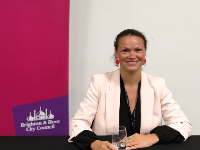 Leader of the Council, Councillor Bella Sankey, sitting at a desk in front of a Brighton & Hove City Council banner at one of the 'leader's surgeries' for residents
