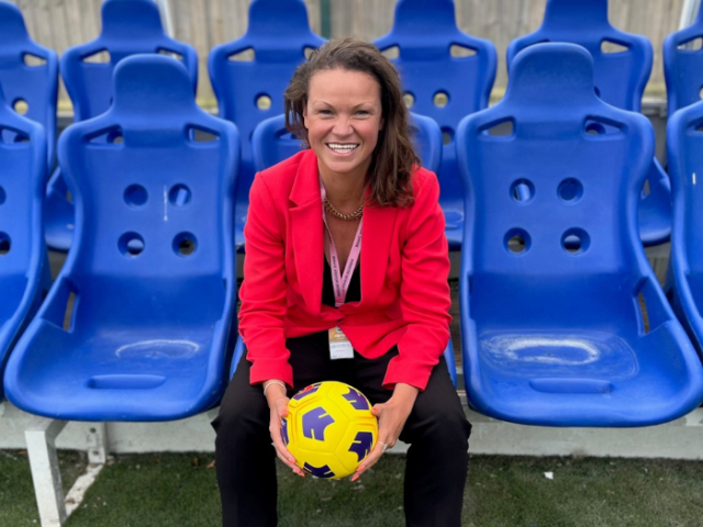 Council Leader Bella Sankey sat on blue football chairs in a red jacket and holding a yellow football