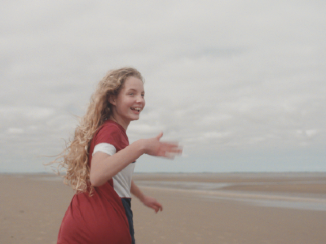 Picture of a young girl, in a red t-shirt, smiling while playing on the beach