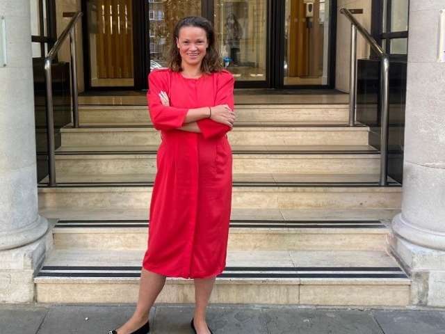 Image shows Brighton & Hove City Council leader Bella Sankey standing outside a building with stairs and a pillar on each side