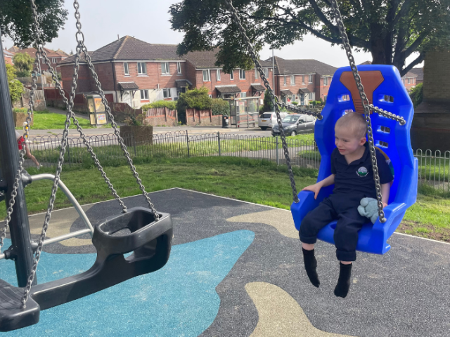 Photograph of a young boy smiling and swinging on an accessible hammock swing.