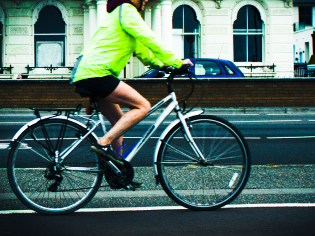 Person in a hi-vis jacket cycling on a bike on the road.