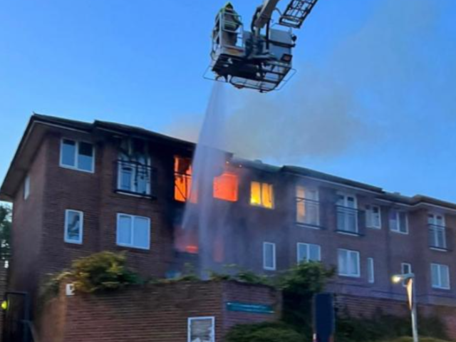 Image shows a fire at a block of flats with firefighters spraying water from a fire engine platform