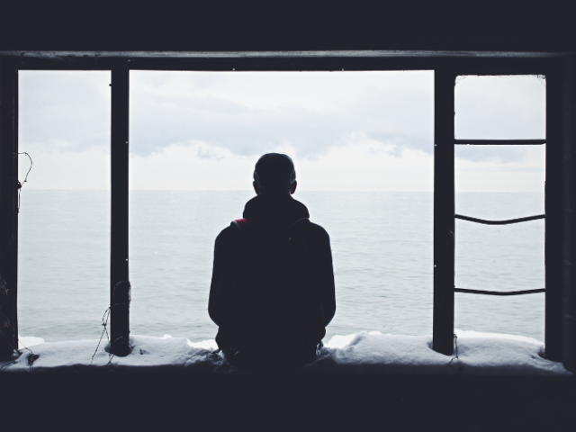 Photo of a man on his own staring out a window at the sea