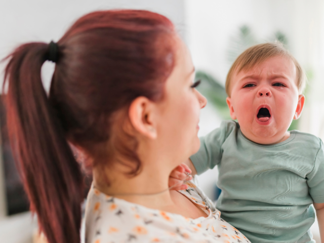woman holding baby who is coughing and has red face 