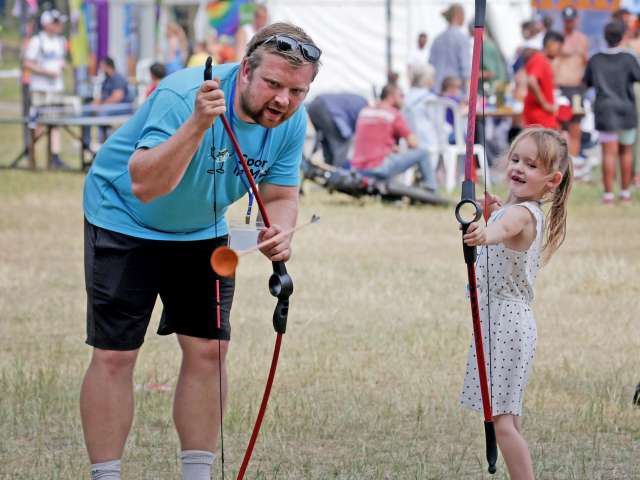 adult man and young girl in field learning archery