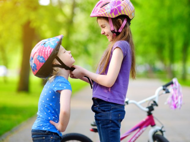 Two children wearing cycle helmets in a park standing near a bicycle