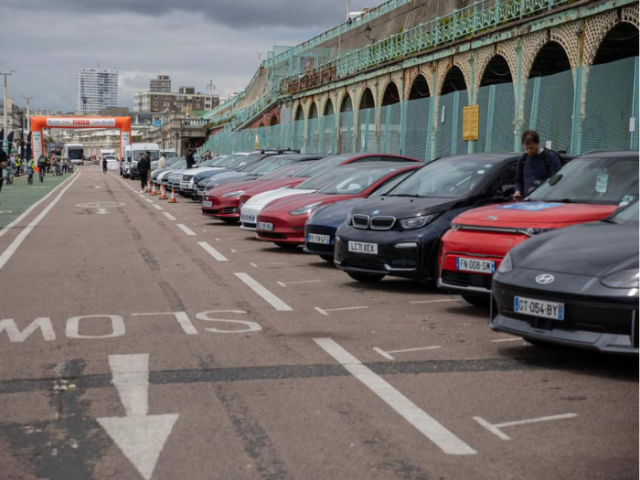 A picture of a road with a row of cars parked on one side