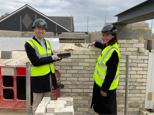 The image shows Council Leader Bella Sankey and Councillor Jacob Allen donning hi vis vests and hard hats while laying bee bricks at the new Brickfields supported living scheme.