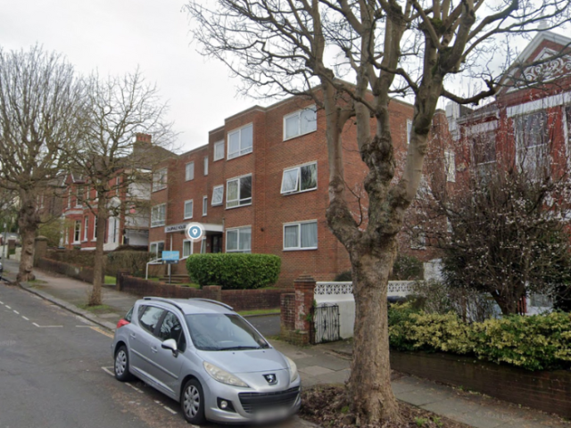A picture of a tree on the side of a road. There is a car parked next to it and houses in the background