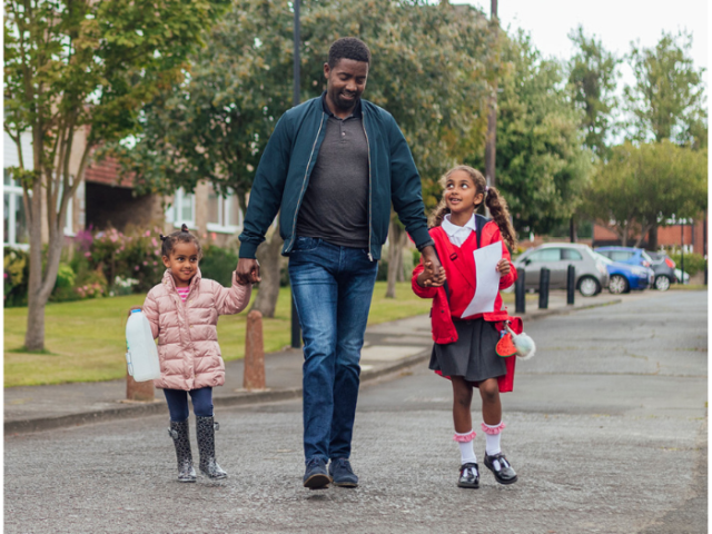 A man walking on a road holding hands with two children