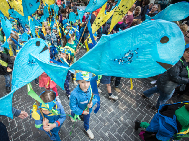 Picture of a child carrying a large blue fish in the Children's Parade. By Vic Frankowski.