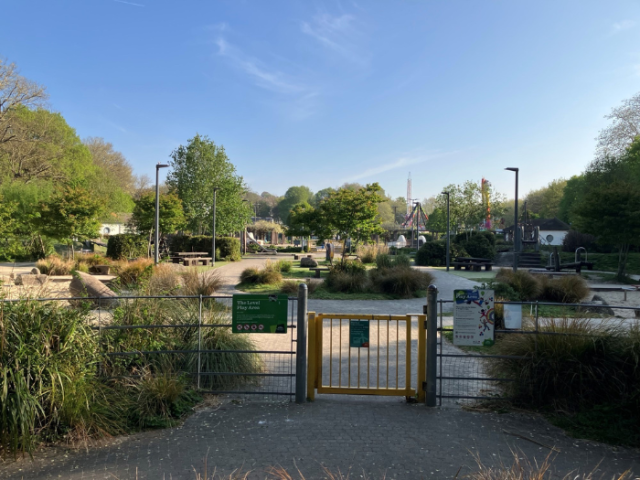 A picture of a playground with bushes, trees and a gate