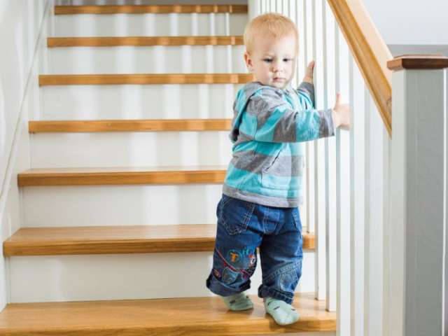 A young child walking down the stairs holding on to the banister