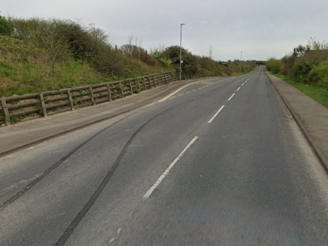 A picture of a road with pavement and fence either side