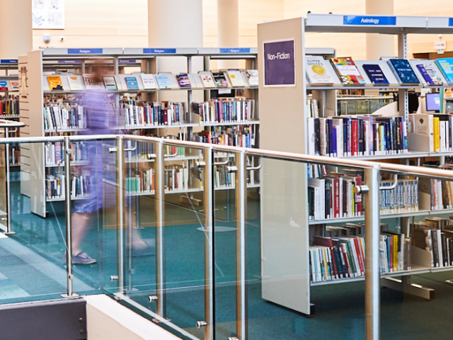 A photo of a person in motion walking towards a row of library shelves