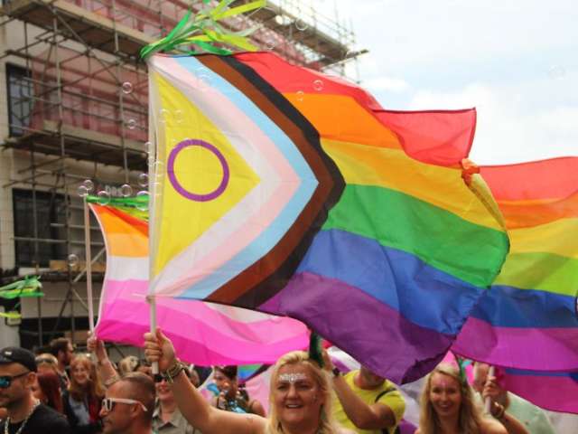 a woman marching the Pride parade holding a Pride rainbow flag