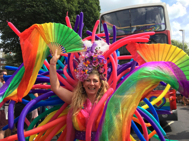 A person wearing a bright and colourful outfit, smiling and standing in front of a bus