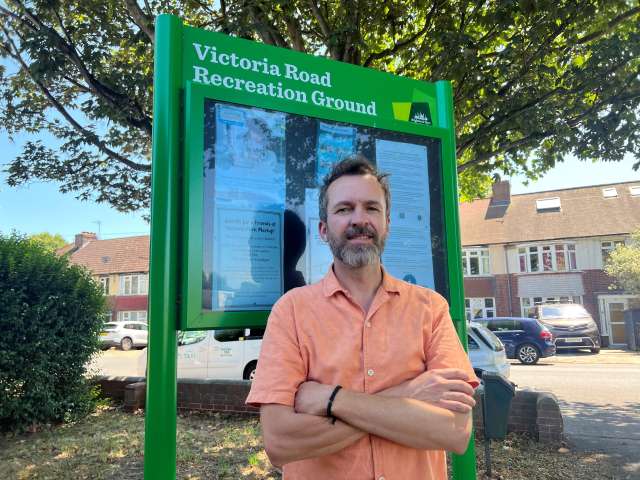Councillor Tim Rowkins stood in front of a green community noticeboard with Victoria Road Recreation Ground at the top.
