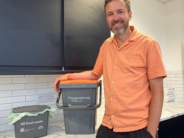 Councillor Tim Rowkins wearing an orange short sleeved shirt, with the kitchen caddy on the left and the larger outdoor caddy on the right