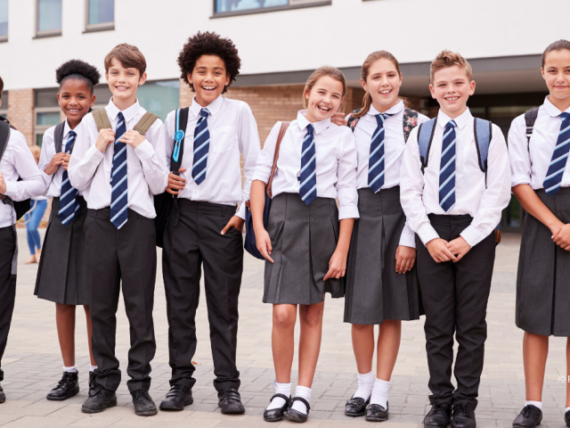 8 children in school uniform standing in a line outside a school building