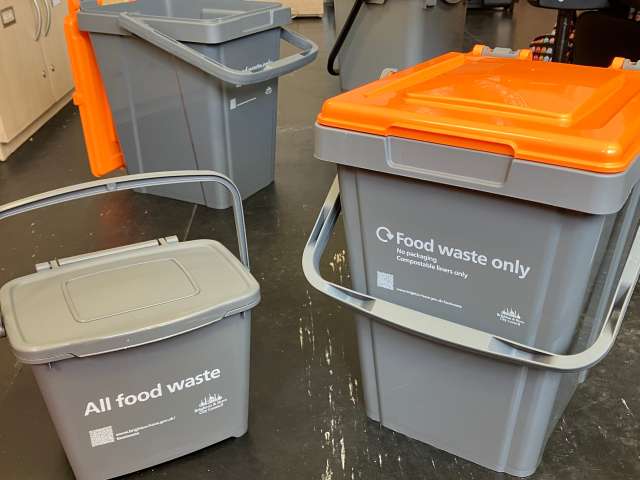 Small grey kitchen caddy alongside larger outdoor food waste caddies with an orange lid