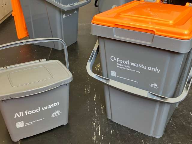 Small grey kitchen caddy alongside a larger outdoor food waste caddy with an orange lid