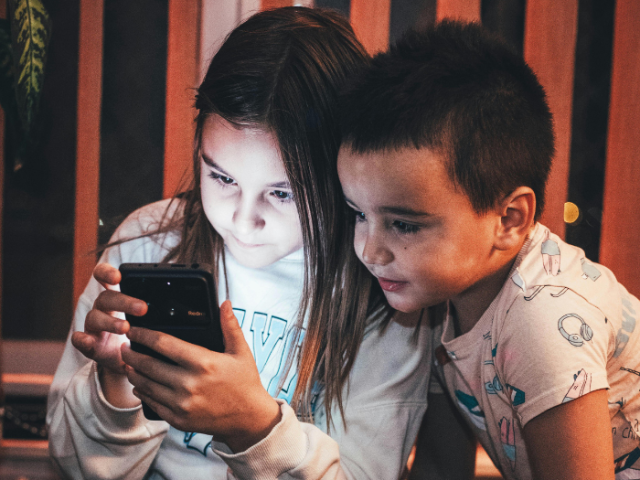 A photo of two children looking at a smartphone