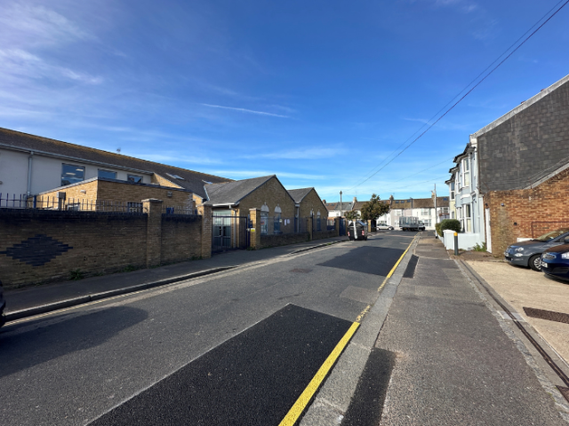 A picture of a road, with a school in the background beneath a blue sky