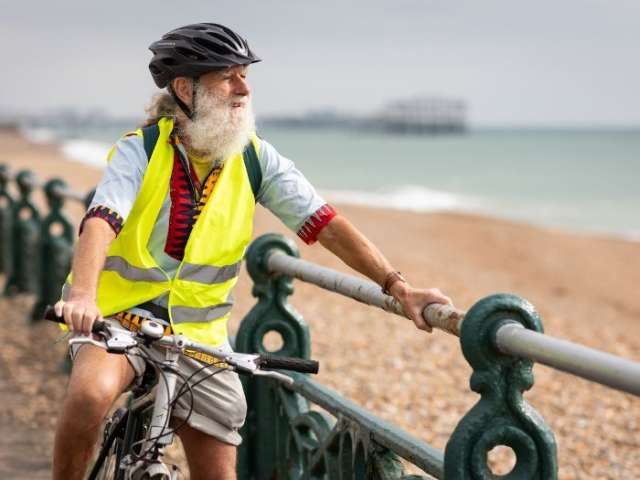 A man with a grey beard on a bike holding onto the railing looking out to sea in Brighton 