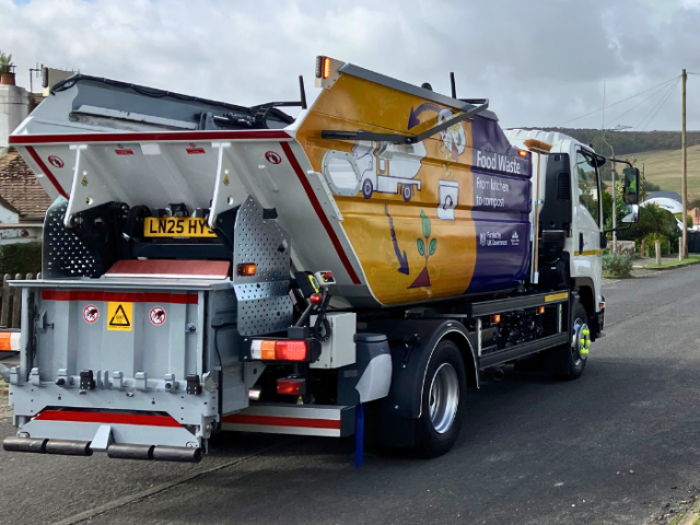Back view of a branded food waste truck on a street.