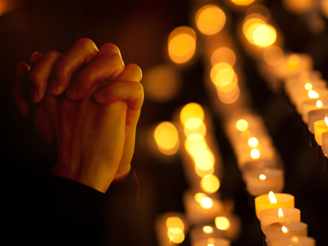The image shows hands in prayer, surrounded by lit candles.