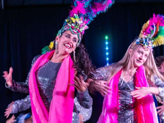 Two women dancing with brightly coloured outfits and headdresses on stage
