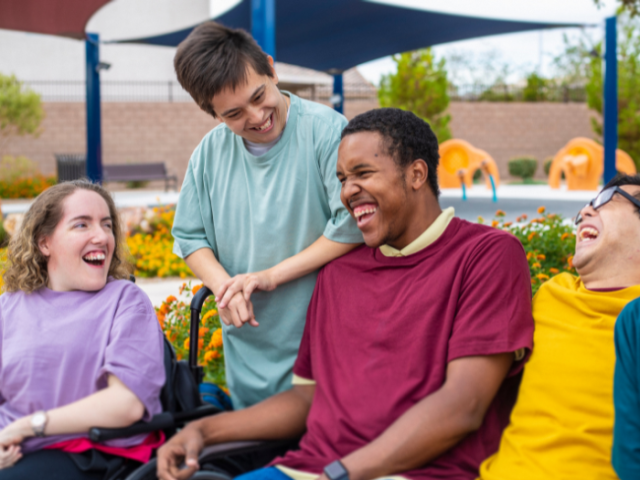 The image shows 4 young people with disabilities laughing together and having a nice time.