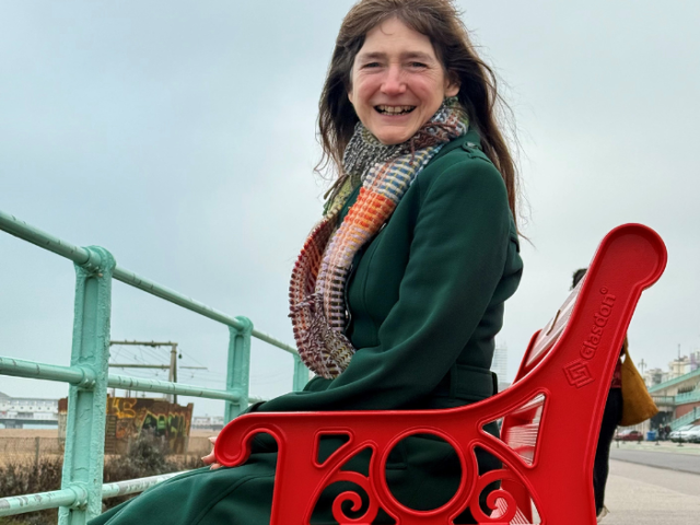 Cllr Mitchie Alexander sitting on the red British Heart Foundation bench