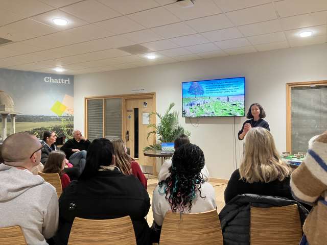 Hannah presenting at the film premiere, with the big screen in the background, and people sitting in the foreground with their backs to the camera.