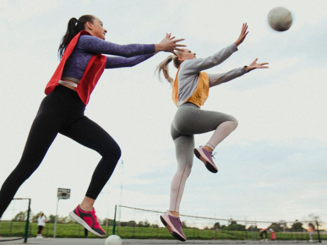 Two women compete for a netball on a netball court