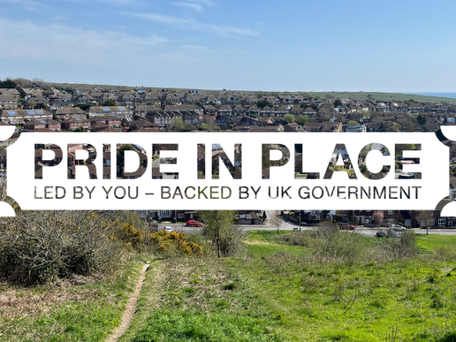 The image shows a photo of Whitehawk from a hill on a sunny day, overlaid with graphics saying: 'Pride in Place. Led by you - backed by UK government.'