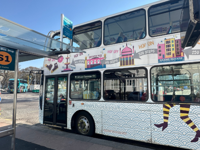 a bus at a bus stop. The bus has iconic images of Brighton & Hove on it