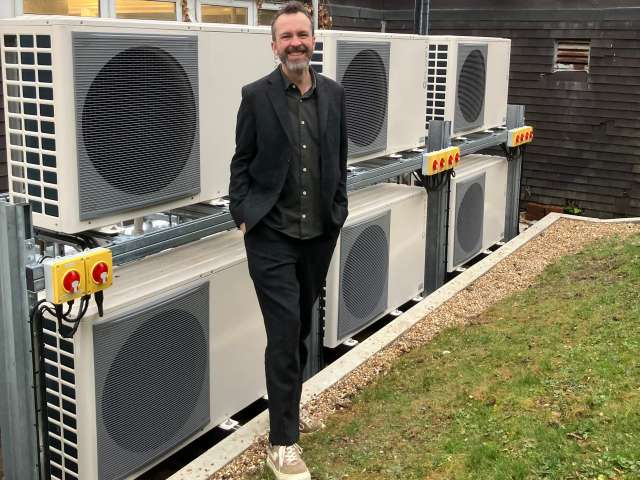 Councillor Tim Rowkins standing in front of 6 heat pumps that have been installed at Peter Gladwin Primary School