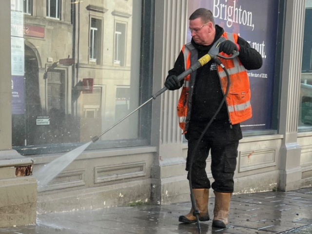 Man in orange hi-vis jacket jet washing the pavement.