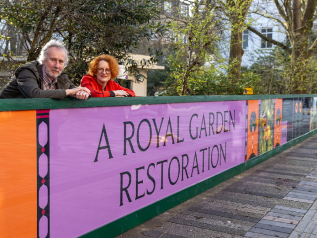 Brightly coloured information board with a man and a woman stood behind it.