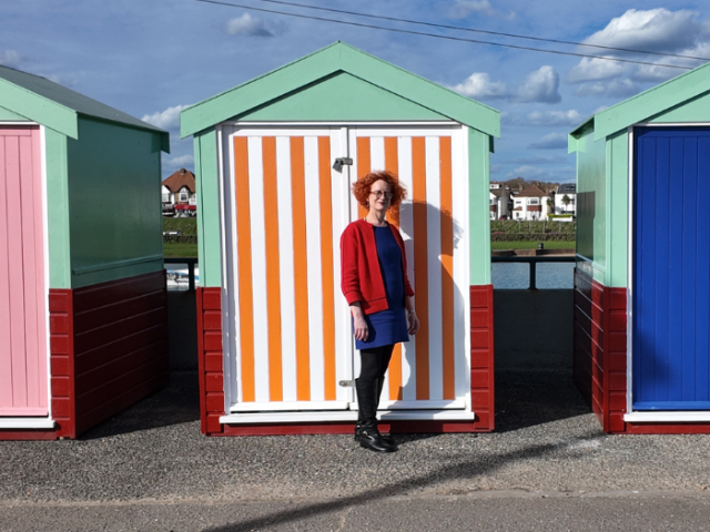 Councillor Birgit Miller standing in front of the beach huts on Hove seafront